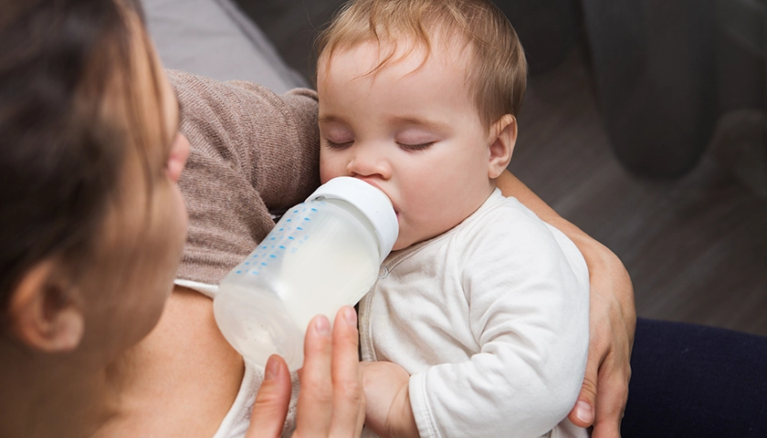 Bebé  en brazos de su madre tomando un biberón de leche previamente calentado.webp
