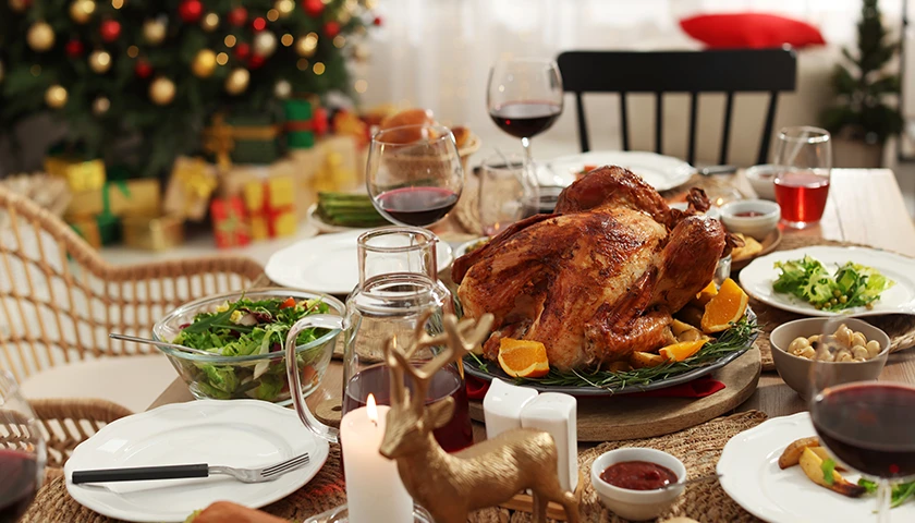 Mesa navideña con comida copiosa, ensaladas y vino, lista para una celebración familiar junto al árbol de Navidad..webp