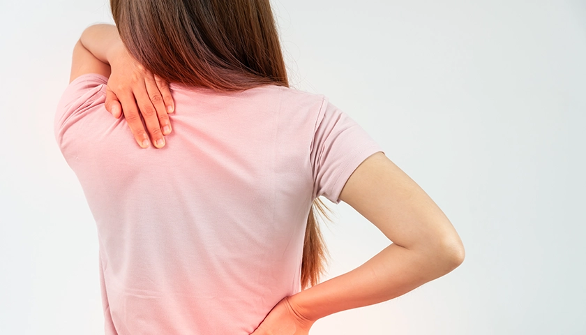 Mujer con dolor en la zona dorsal sujetándose la espalda con la mano..webp
