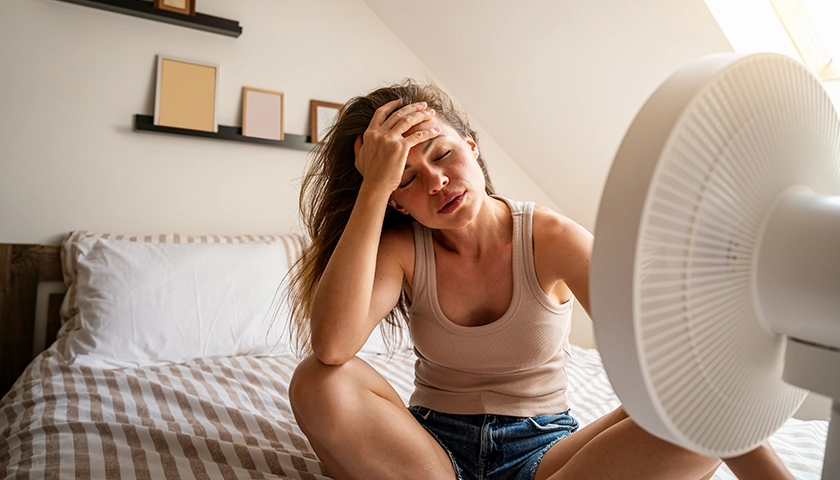 Mujer con mareo por calor en verano delante de un ventilador.webp