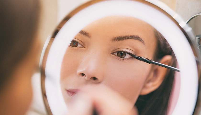 Mujer maquillándose para Navidad con máscara de pestañas frente al espejo.webp
