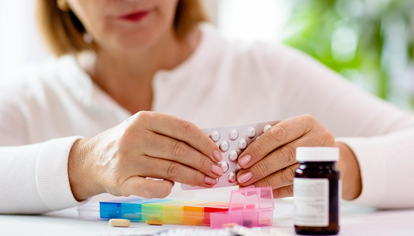 Mujer organizando medicamentos en un pastillero para conservarlos en días de calor.webp